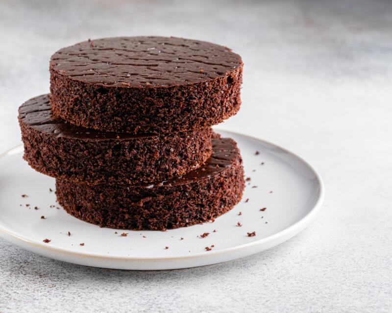 Chocolate sponge cake (biscuit) cut in circle layers stacked on ceramic plate with crumbs