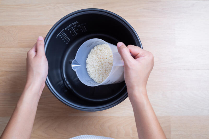 Woman hand is pouring jasmine rice into a rice cooker