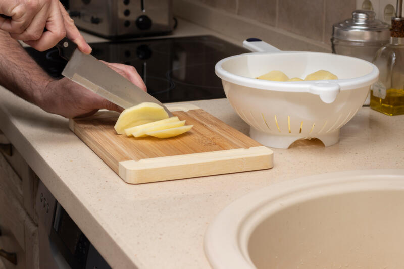 A man slicing potatoes, on top of a wooden board