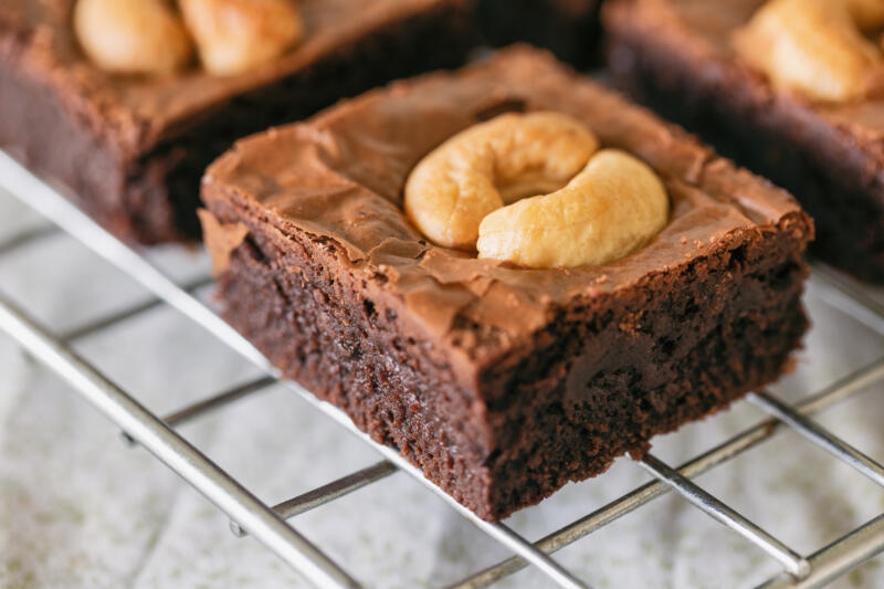 Freshly baked chocolate fudge brownies topped with cashew nuts resting on the rack