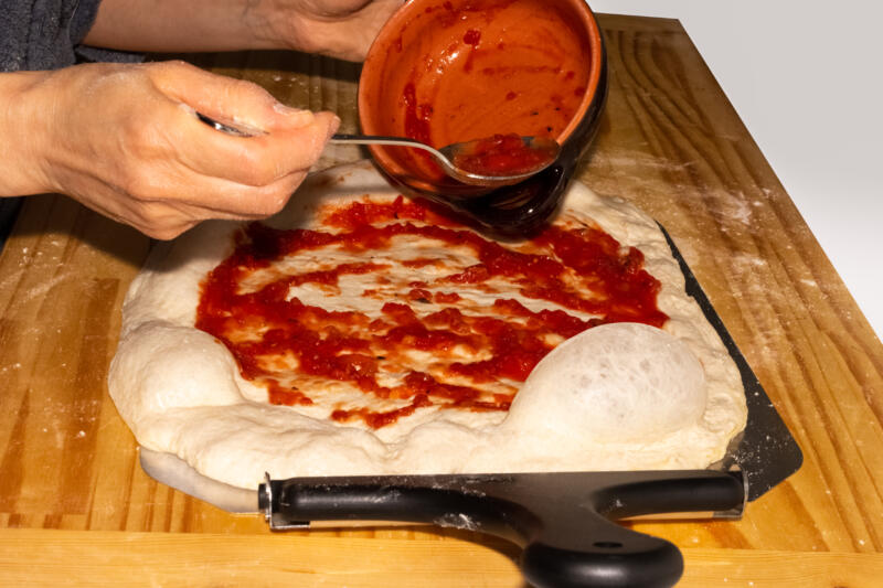 Woman dressing a pizza with a tomato sauce