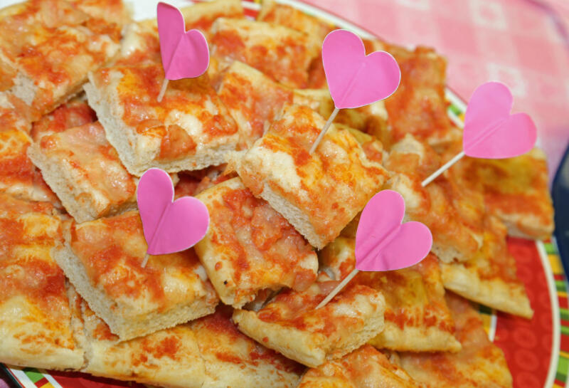 A plate of pizza slices with heart-shaped flags at the little girl's party