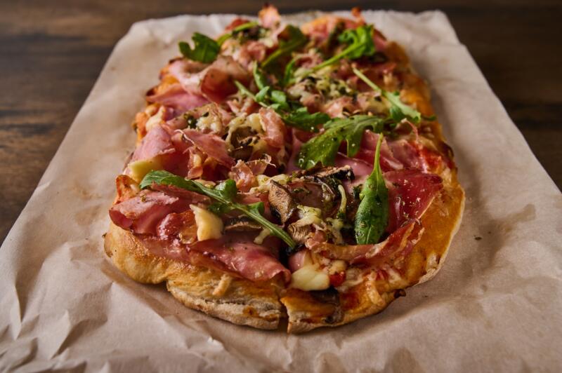 Close-up of rectangular Roman pizza with prosciutto, mushrooms and arugula