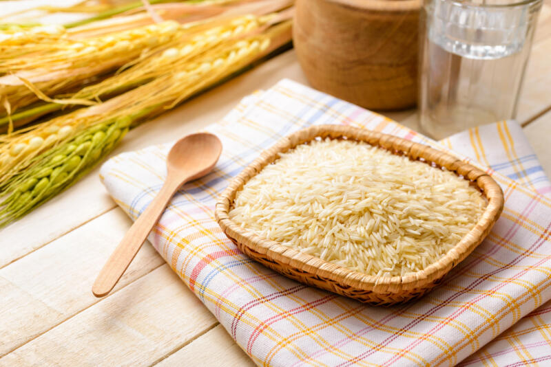 Uncooked basmati rice, extra long type, in a little plate on a towel put on a wooden table.