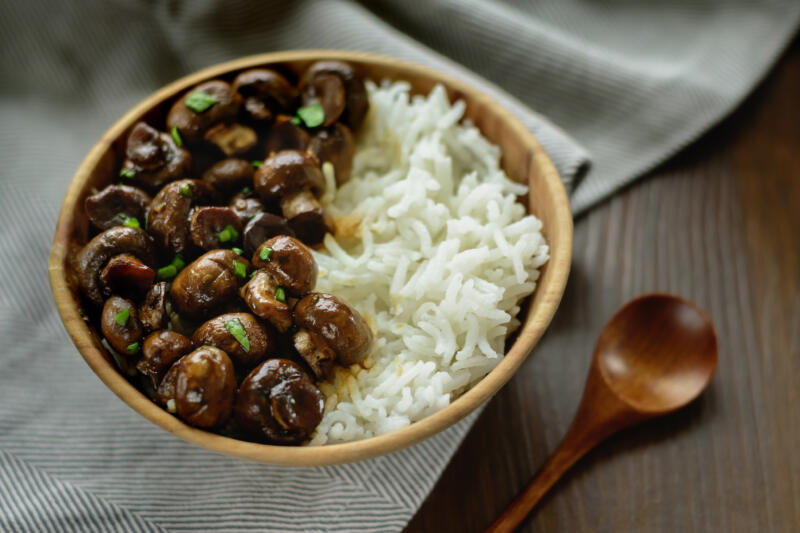 Sauteed whole white mushrooms with basmati rice in wooden bowl on table