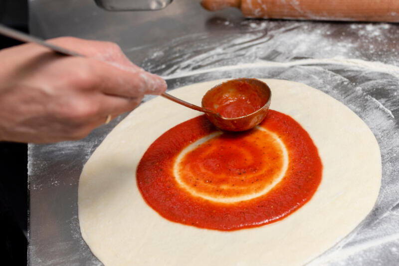 Chef putting tomato sauce on a prepared pizza dough