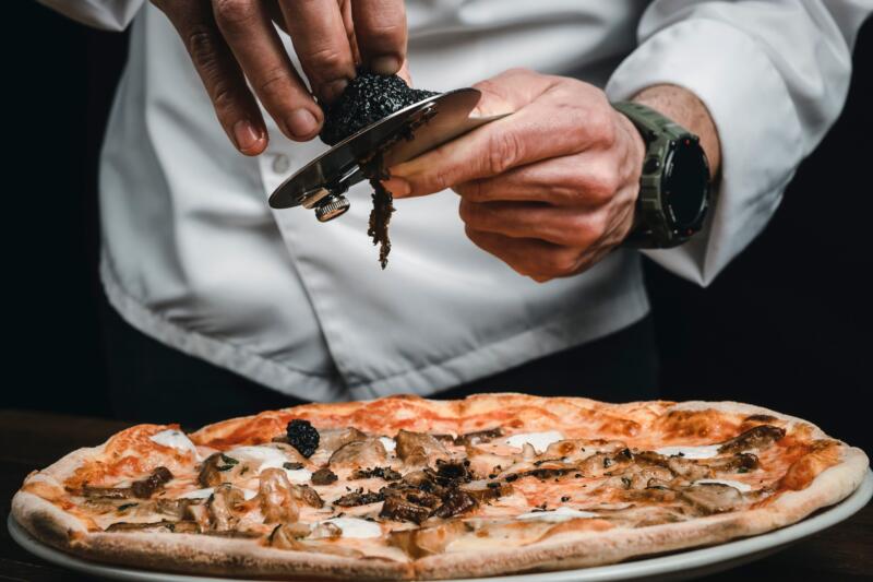 Chef slicing black truffles over a pizza