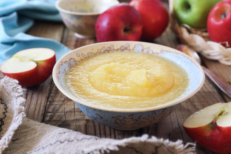 Unsweetened applesauce in a plate and fresh apples on a table
