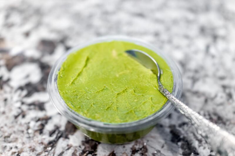 A container of mashed avocado on a grey table