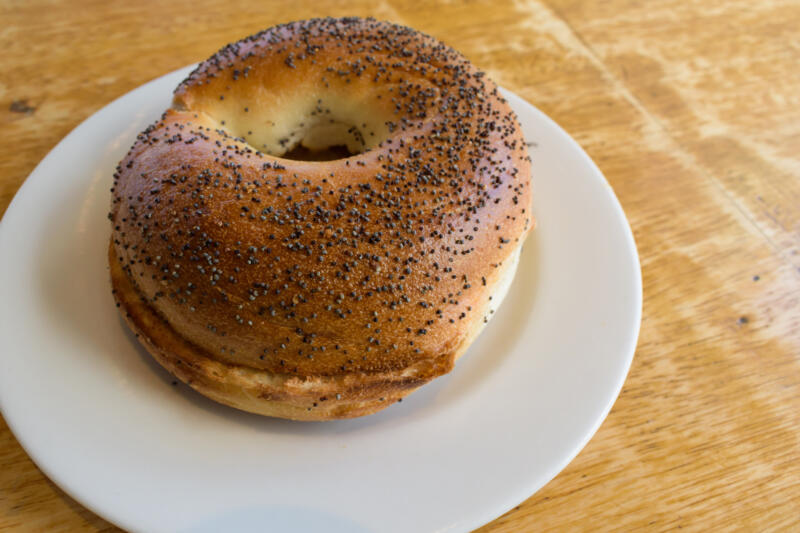 Toasted poppy seed bagel cut in half in a white saucer plate placed on a table