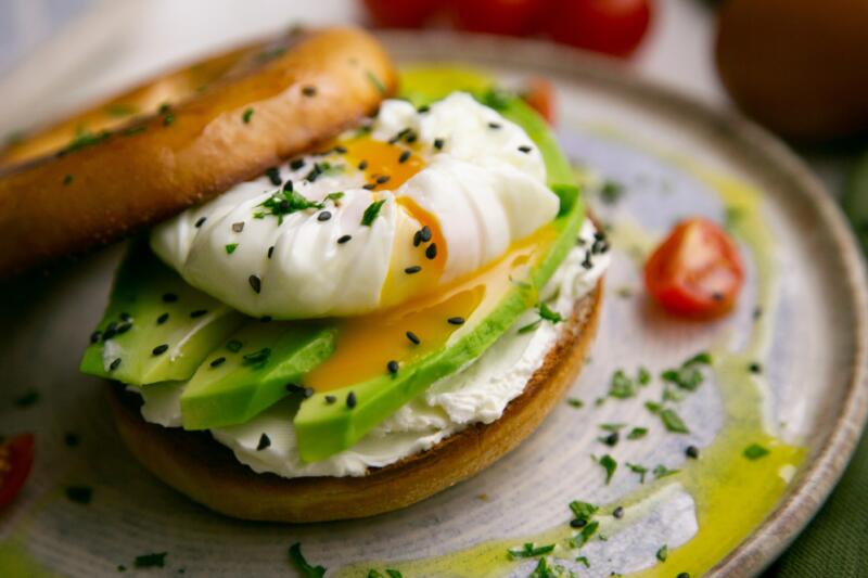 A vegan brunch - toasted bagel with cream cheese, avocado, organic cherry tomatoes and poached egg
