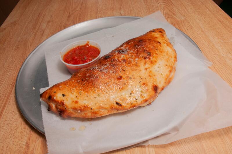 Italian calzone served on a metal plate with a cup of marinara sauce