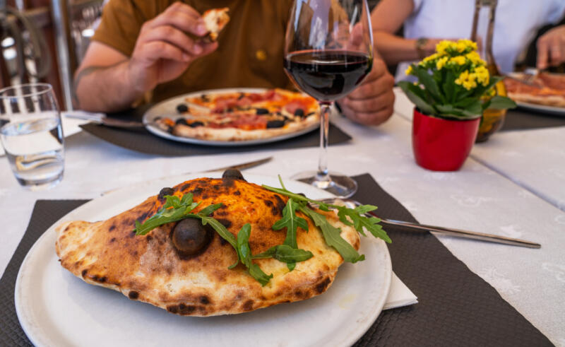 Baked calzone on a plate and a pizza on a table at the restaurant