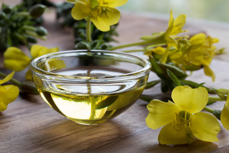 Canola oil in a glass bowl and rapeseed flowers on a table