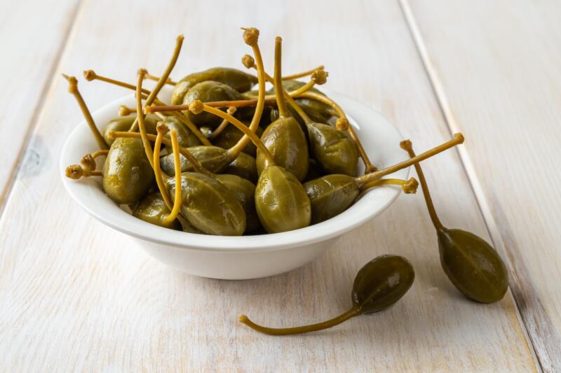 Heap of pickled caper berries in a bowl on a rustic wooden table