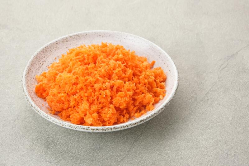 Grated carrots in a small bowl on a grey background