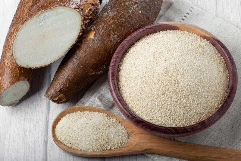 Cassava flour in a bowl and fresh cassava roots on the table