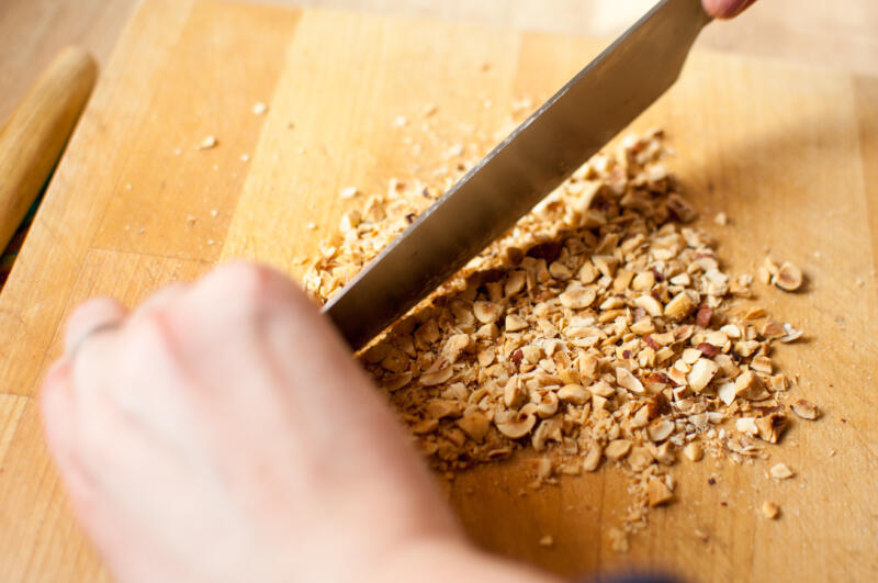 Close up of a chef chopping nuts with a knife on wooden desk