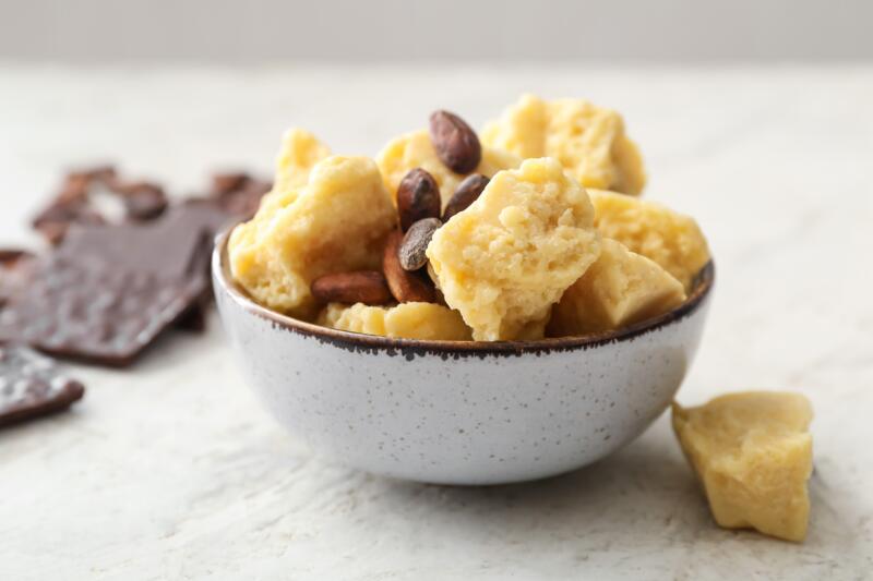 Bowl with cocoa butter and beans on light background