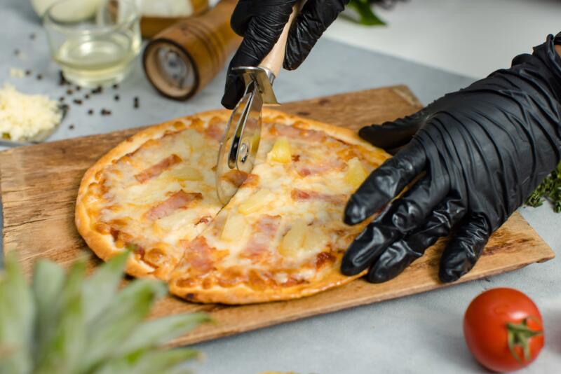 Cutting a pizza into slices wearing gloves and by using a pizza wheel