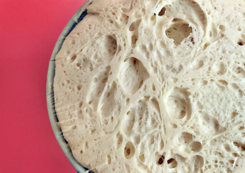Fresh yeast dough for pizza in a metal bowl on a red background