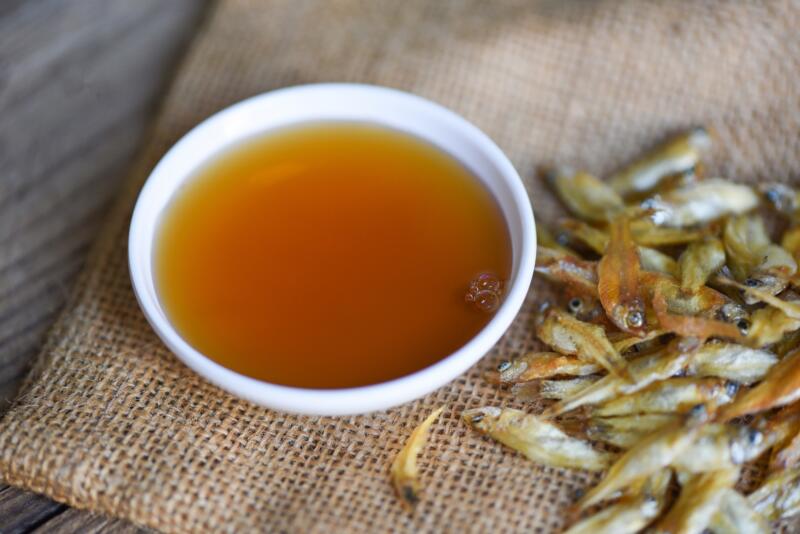 Fish sauce in a white bowl and small dried fish on sack