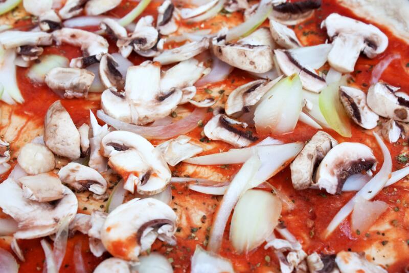 Close-up of uncooked pizza with sliced mushrooms, onions and tomato sauce