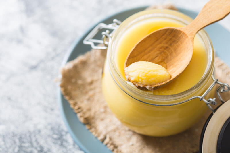 Ghee or clarified butter in a jar and a wooden spoon on a gray table