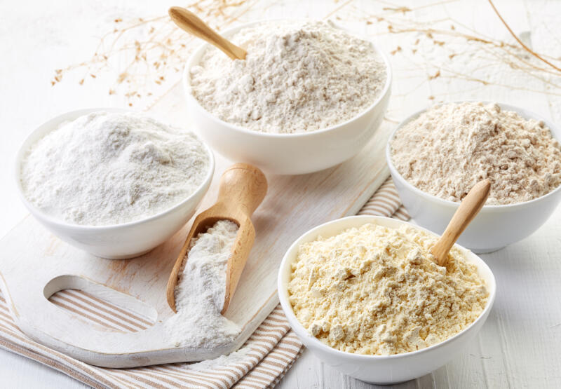 Bowls of different flours such as almond, chick peas, rice, buckwheat, amaranth seeds on white wooden background