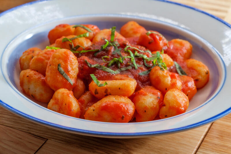 Italian pasta gnocchi with marinara sauce and freshly chopped basil in a plate on a wooden table