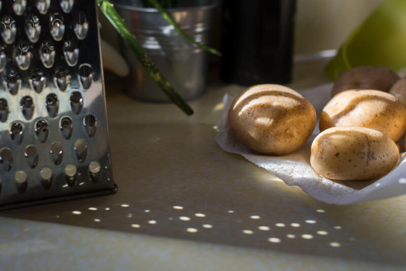 A small pile of potatoes next to a cheese grater on a kitchen counter