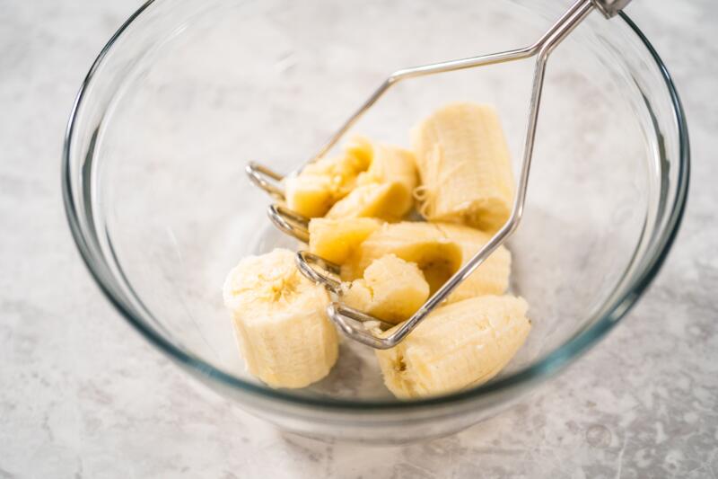 Mashing a banana with a potato masher in a glass bowl