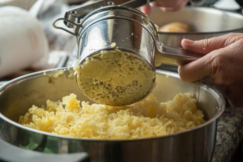 A close-up of the process of making puree with stainless steel rice potato masher
