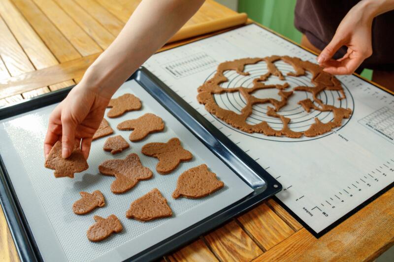Woman hands spreading different shaped homemade cookies on a silicone baking mat on a baking sheet