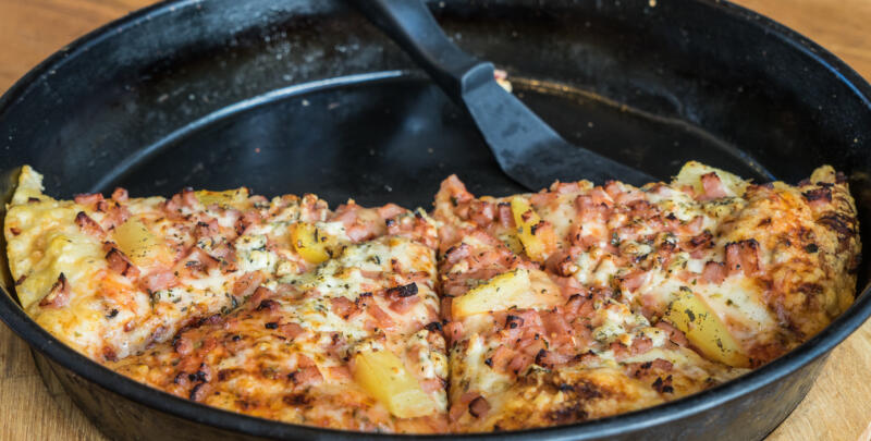 Taking a slice of a reheated pizza in a cast iron pan