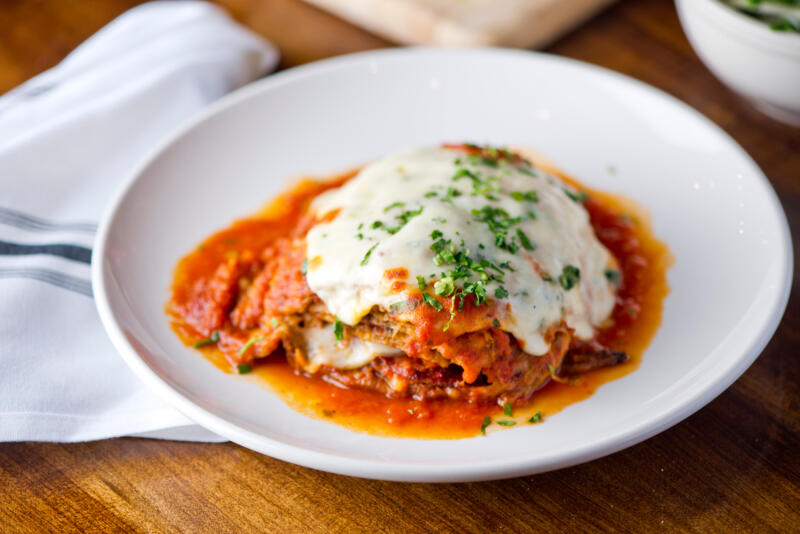 Parmigiana with eggplants, tomato sauce, melted cheese and fresh parsley served in a plate