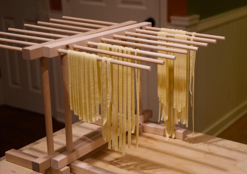 Fresh pasta drying on a wooden pasta tree in a home kitchen
