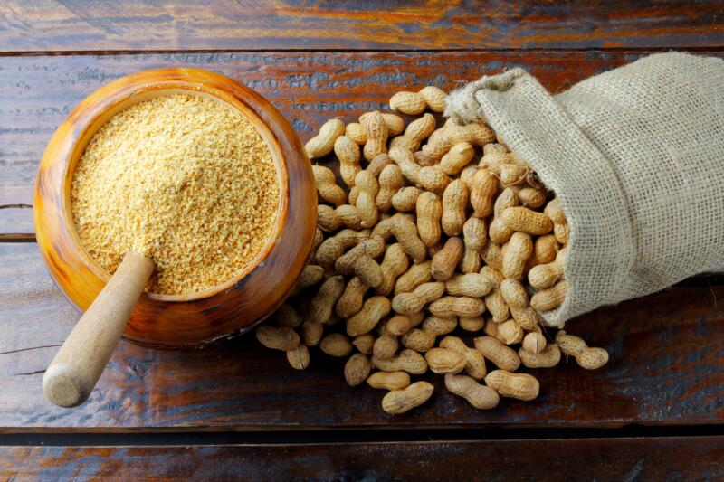 Cashew flour in a bowl and fresh whole peanut in a bag on the table