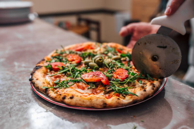 Cook cutting a pizza with a pizza wheel in a kitchen