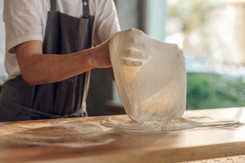 Skilled chef stretching a pizza dough for a pizza