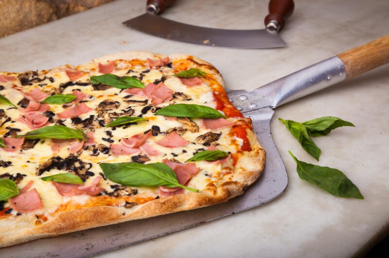 Freshly baked pizza on a metal pizza peel on a kitchen counter