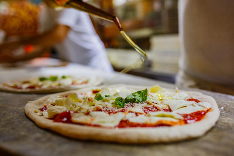 Cook putting a drizzle of oil on a pizza ready to be baked