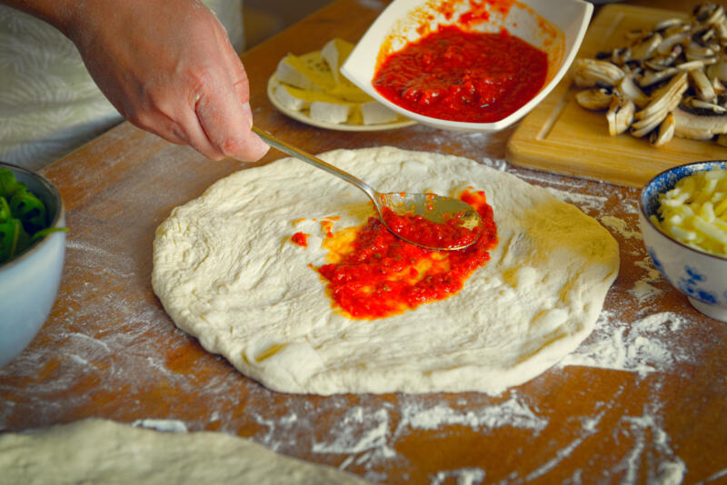 Spreading tomato sauce on a pizza dough