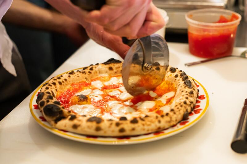 Pizza maker cutting a pizza with a pizza wheel