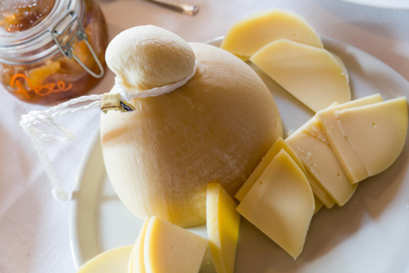 The whole Provolone cheese and some cut slices on a big plate on a table