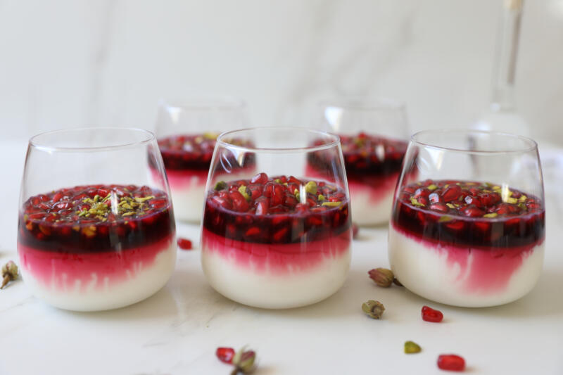 Milk pudding topped with pomegranate seeds, juice, pistachios & rose water