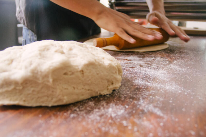 Homemade pizza dough and woman rolling some dough on a table