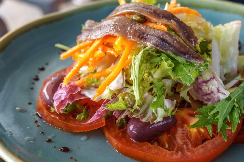 Fresh green and violet lettuce, anchovies, tomato and olives, virgin olive oil in a plate