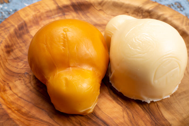 White, natural and smoked Scamorza cheeses on a wooden service plate