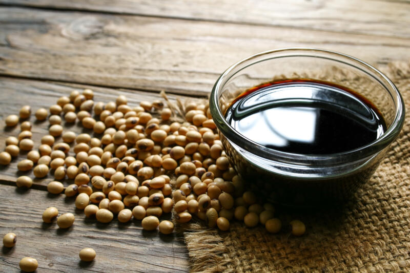 Soy sauce in a bowl and soybeans on a wooden table